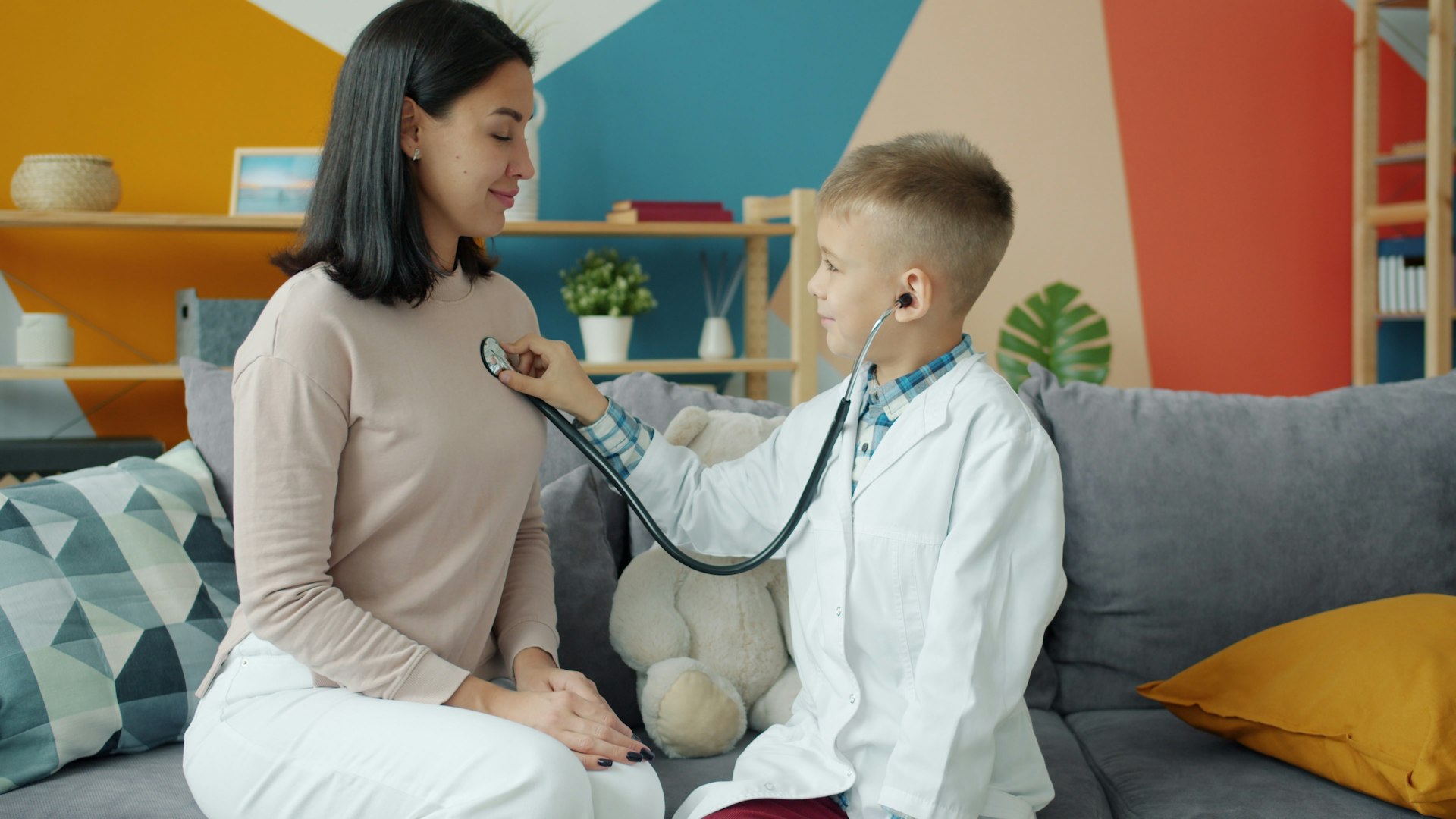 Boy in doctor's coat listens to mother's chest